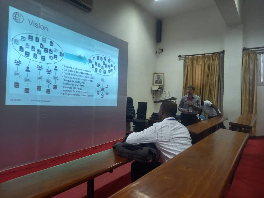 A person standing in the lecture hall in front the projection of a powerpoint presentation.